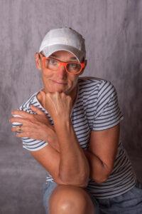 portrait d'une femme avec une casquette assise sur un escabeau en bois ses mains tiennent sa tête photographe de portrait- krystyne ramon - home studio photos