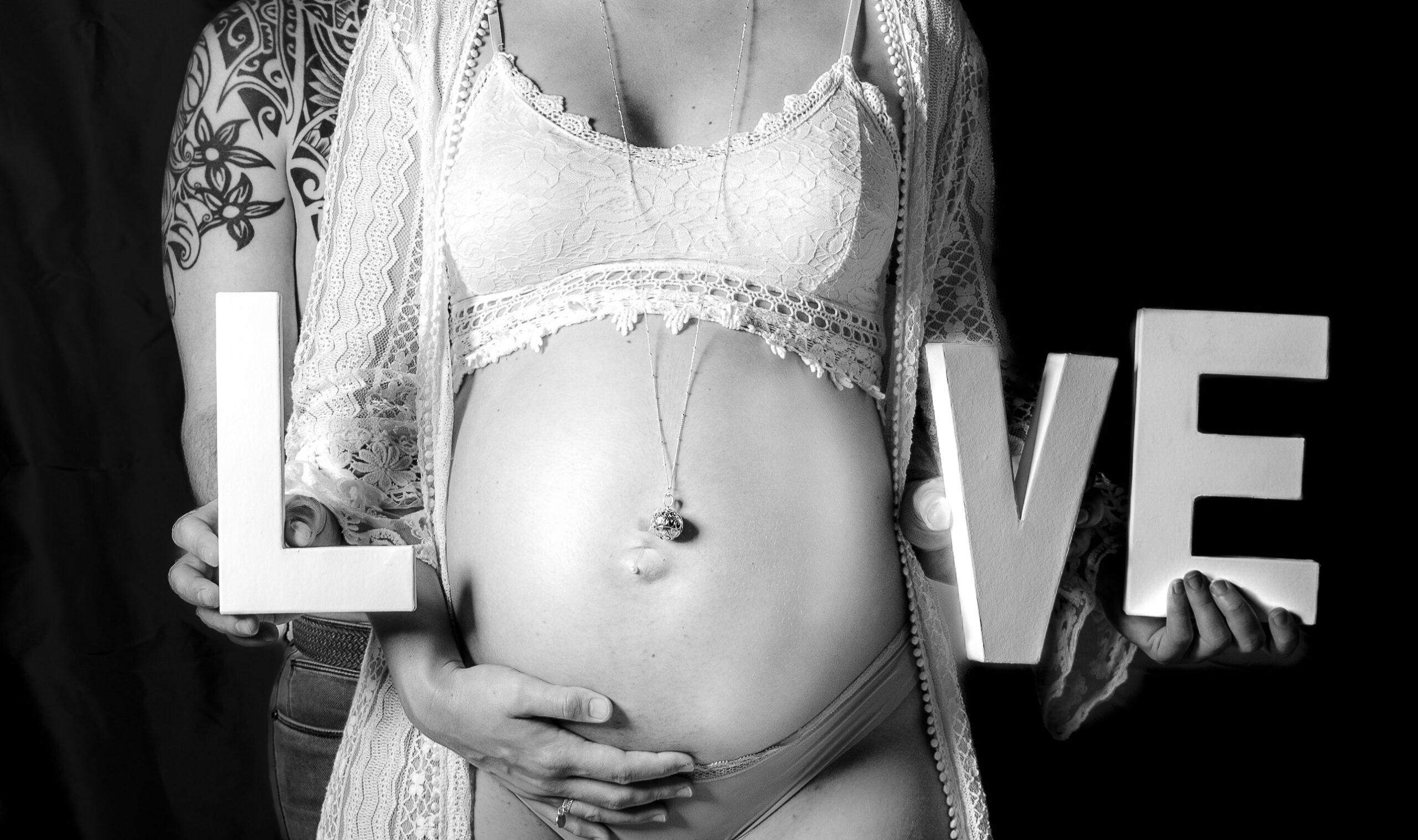 photo grossesse couple de futurs parents elle est devant lui et tient les lettres love devant son ventre