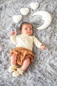 nouveau-né couché sur un tapis avec au dessus une lune et trois petits cœurs -photographe de naissance- krystyne ramon