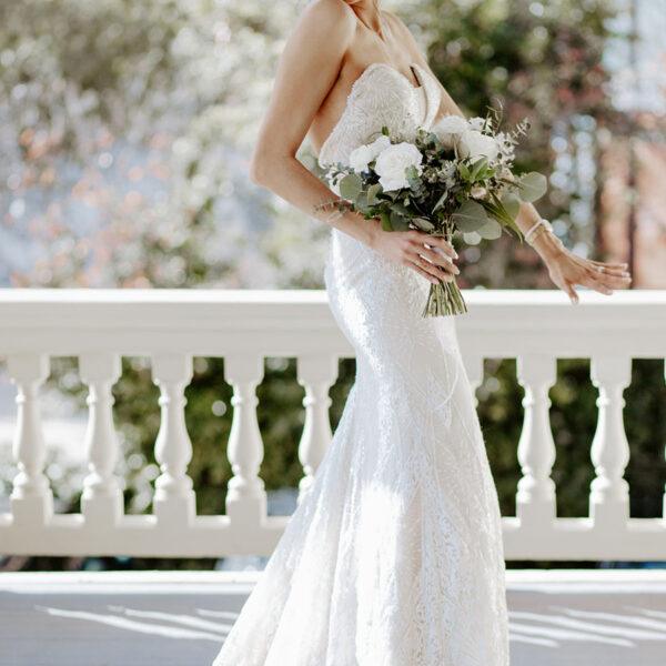 Mariée devant une balustrade un bouquet a la main elle sourit- photographe de mariage