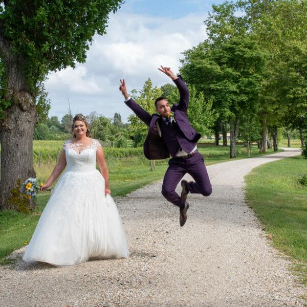 couple de mariés sur un chemin dans le vignoble lui il saute et elle marche a ses cotés- photographe de mariage- krystyne ramon