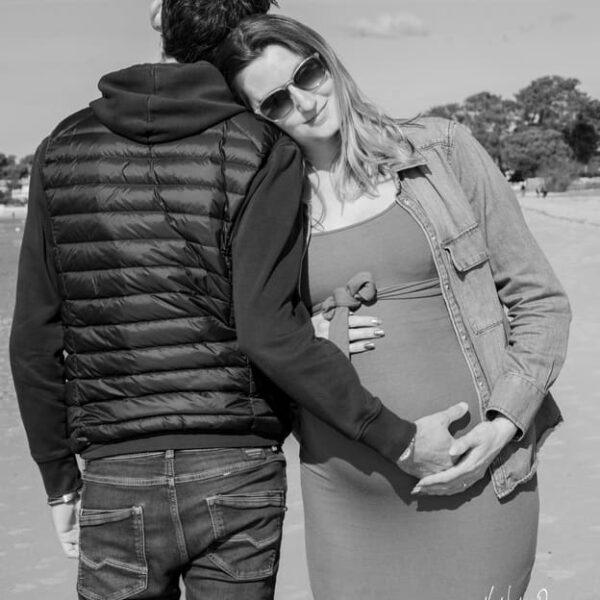 Futur parents sur la plage face et dos lui posant la main sur son ventre -photographe de grossesse- krystyne ramon
