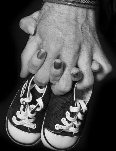 Main dans la main un couple tient une paire de chaussure pour bébé -photographe de naissance- krystyne ramon