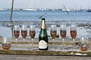 séance EVJF huit verres de champagne au milieu d'une bouteille posés sur une murette devant la mer