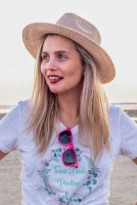 séance EVJF portrait d'une jeune fille sur la plage un chapeau de paille sur la tête et de lunettes rose accrochées sur son tee shirt