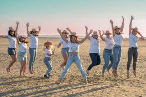 séance photo EVJF dix jeunes filles sur la plage sautent les bras en l'air
