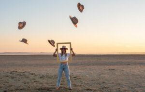 séance EVJF, Je ne femme sur la plage le buste et la tete dans un cadre et des chapeaux ont été en lancés au dessus d'elle