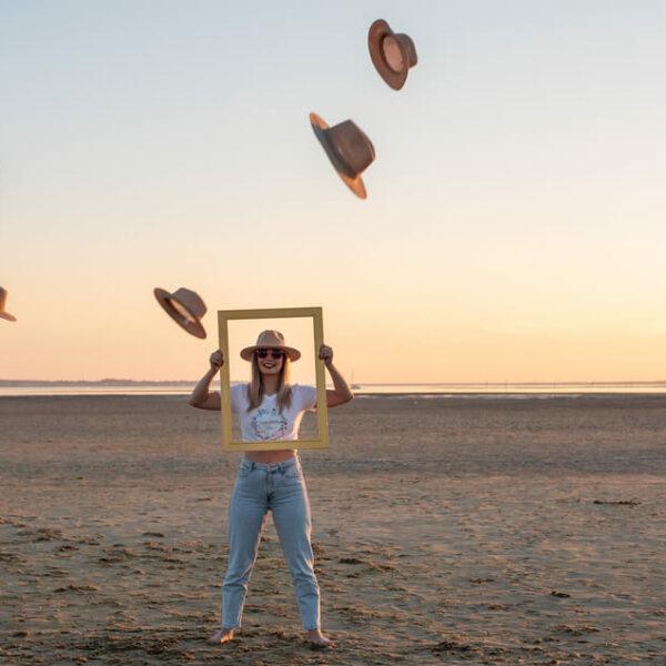 séance EVJF, Je ne femme sur la plage le buste et la tete dans un cadre et des chapeaux ont été en lancés au dessus d'elle krystyne ramon - home studio photos