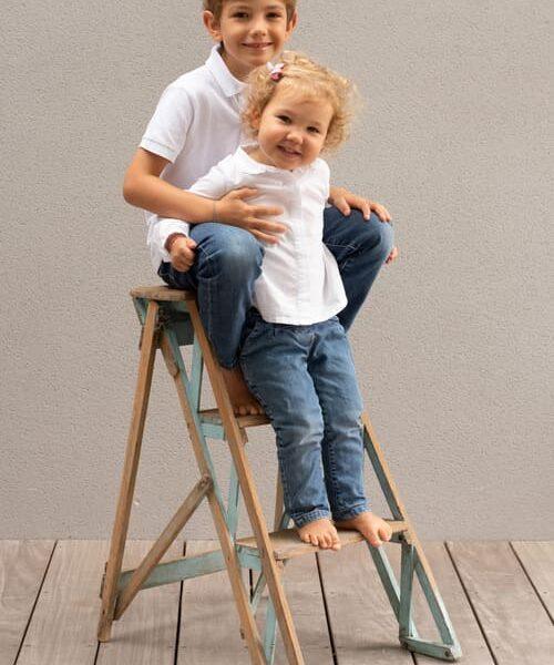 portrait de deux enfants le garçon assis sur un escabeau et sa petite soeur debout sur une marche krystyne ramon - home studio photos
