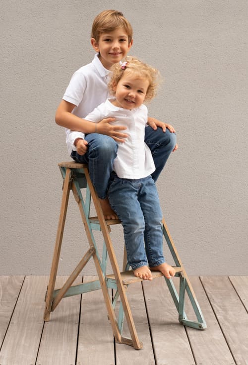 portrait de deux enfants le garçon assis sur un escabeau et sa petite soeur debout sur une marche krystyne ramon - home studio photos