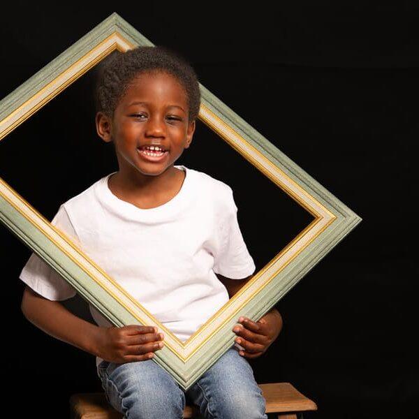 portrait enfant garçon de couleur assis sur un escabeau en bois la tête dans un cadre en bois krystyne ramon - home studio photos