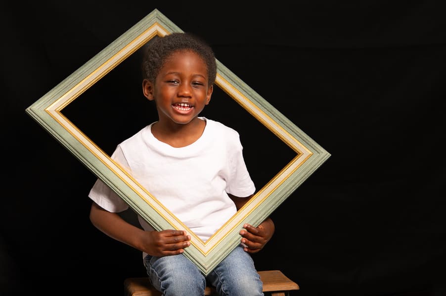 portrait enfant garçon de couleur assis sur un escabeau en bois la tête dans un cadre en bois krystyne ramon - home studio photos