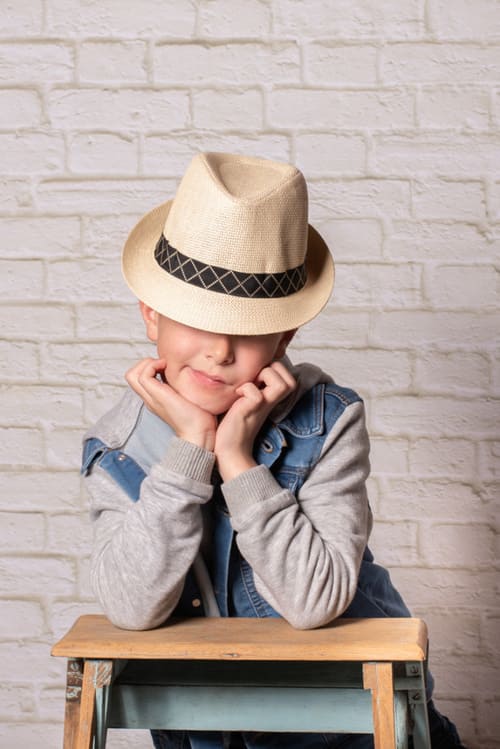 portrait du jeune garçon avec un chapeau on ne lui voit pas les yeux il est accoudé sue un escabeau krystyne ramon - home studio photos