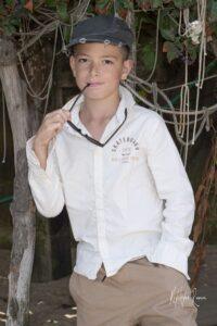portrait enfant jeune garçon avec une casquette appuyé sur un pilotis branche lunette de soleil dans la bouche dans sa poche de pantalon